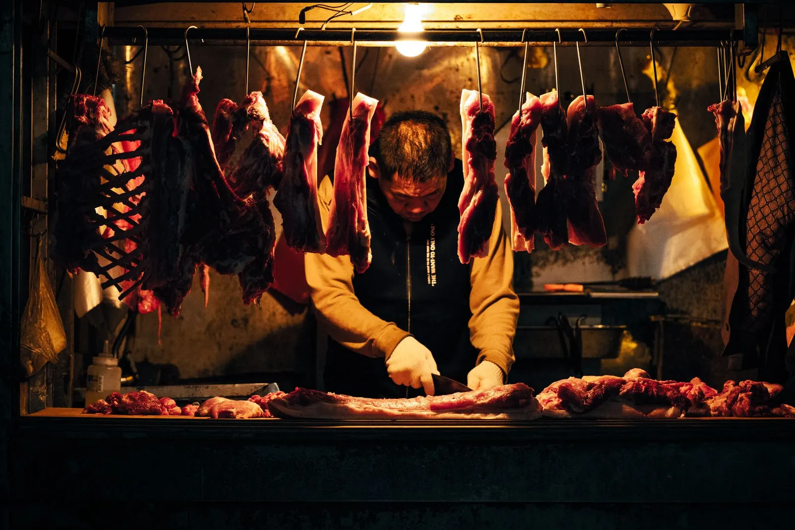 Taiwanese butcher cuts fresh meat under warm lighting in a traditional market stall.